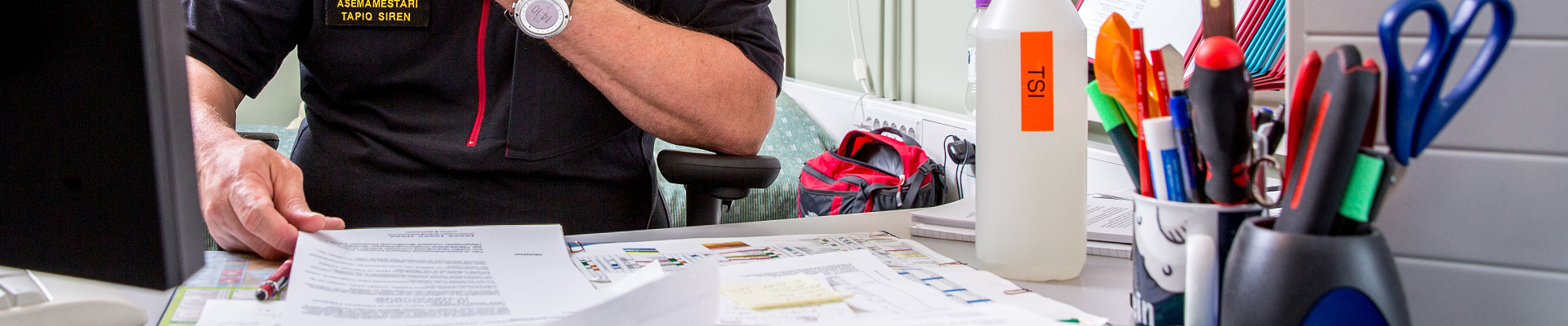Pelastaja tutkimassa työpöydän ääressä papereita